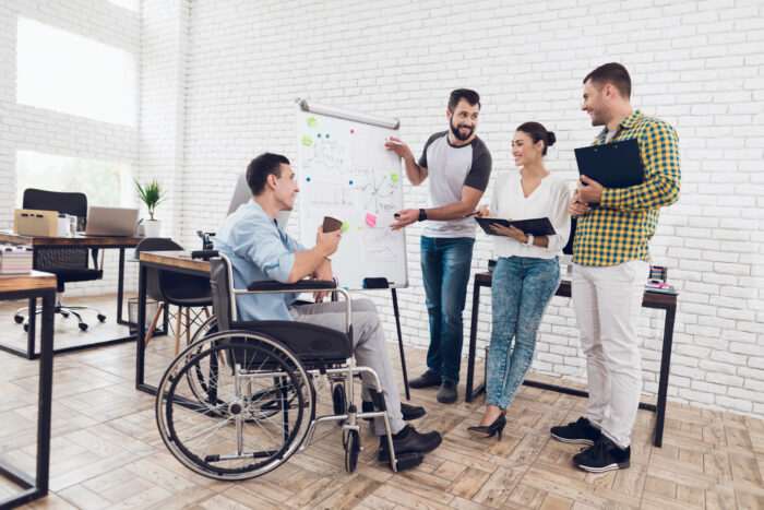 office workers and man in a wheelchair discussing business moments while working in a modern office.